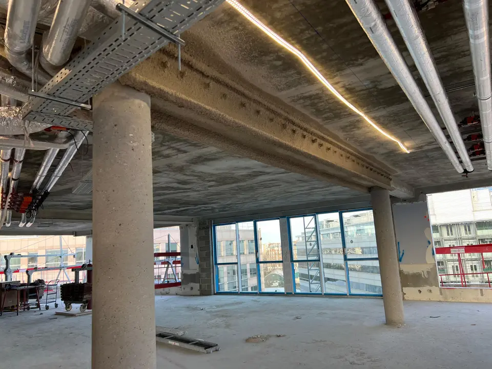 Plateau de bureaux structuré sur poteaux ronds existants, baies vitrées en cours de pose.