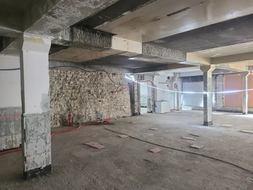 Sous-sol du bâtiment : structure poteaux-poutres béton armé côtoyant les murs de moellons de pierre existants.