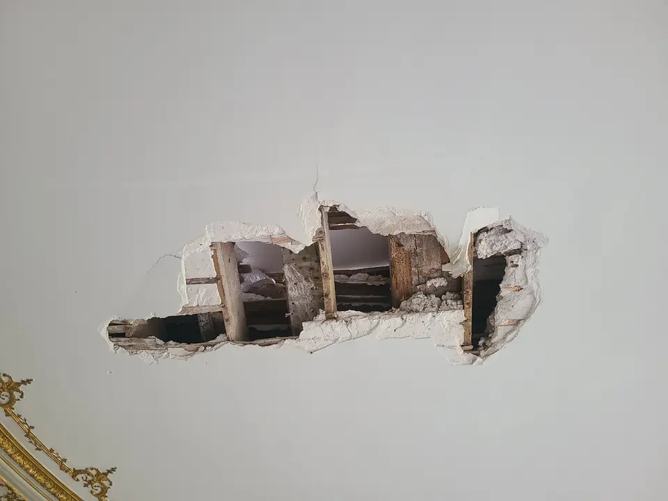 Sondage diagnostic dans un plafond en plâtre : mise à nu des solives bois existantes. Cette photo illustre l'interface entre l'investigation structurelle et la préservation des décors — le sondage est réalisé dans une zone neutre, à l'écart des ornements visibles en bas à gauche.