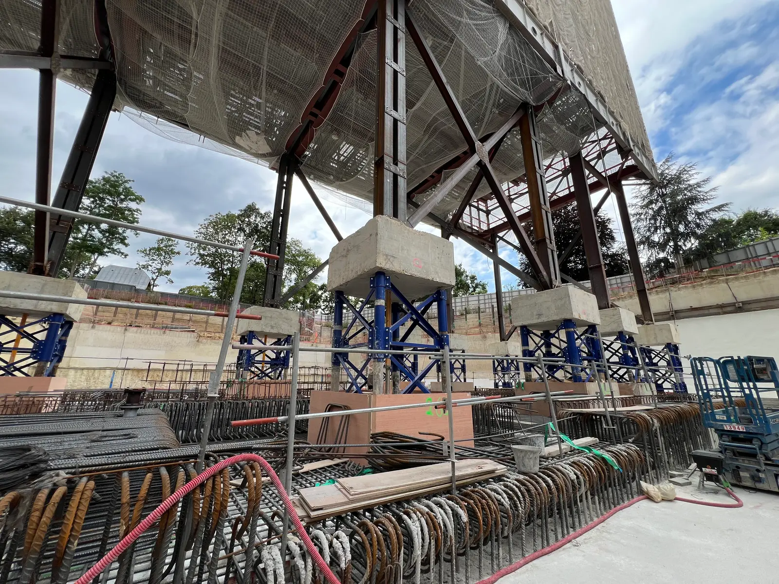 Vue d'ensemble : le bâtiment existant repose sur son dispositif de vérinage, suspendu au-dessus du chantier d'infrastructure en cours de reconstruction.
